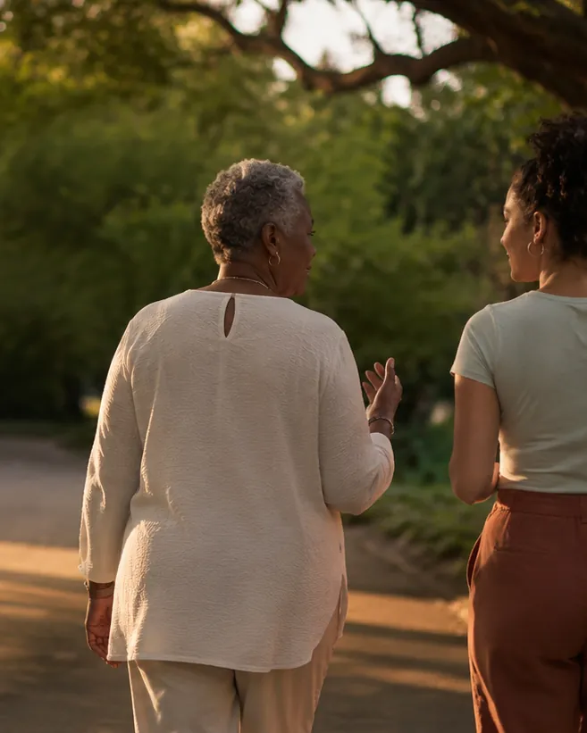 Two women walking a tree-lined road at sunset, deep in conversation.